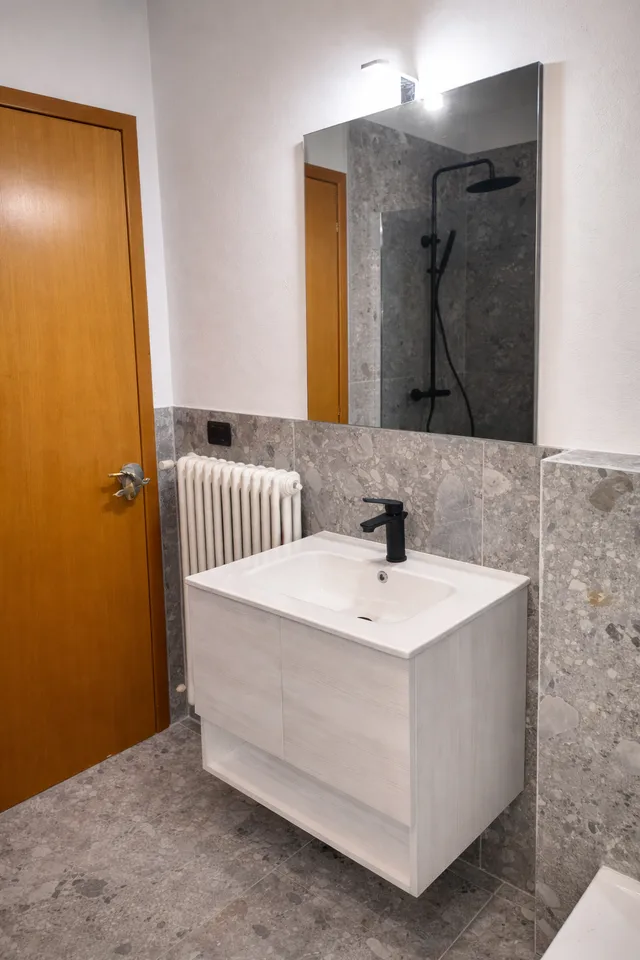 Bagno con rivestimento grigio e mobile lavabo bianco sospeso